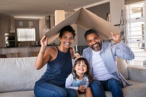 Portrait,Of,Smiling,Family,Sitting,On,Couch,Holding,Cardboard,Roof